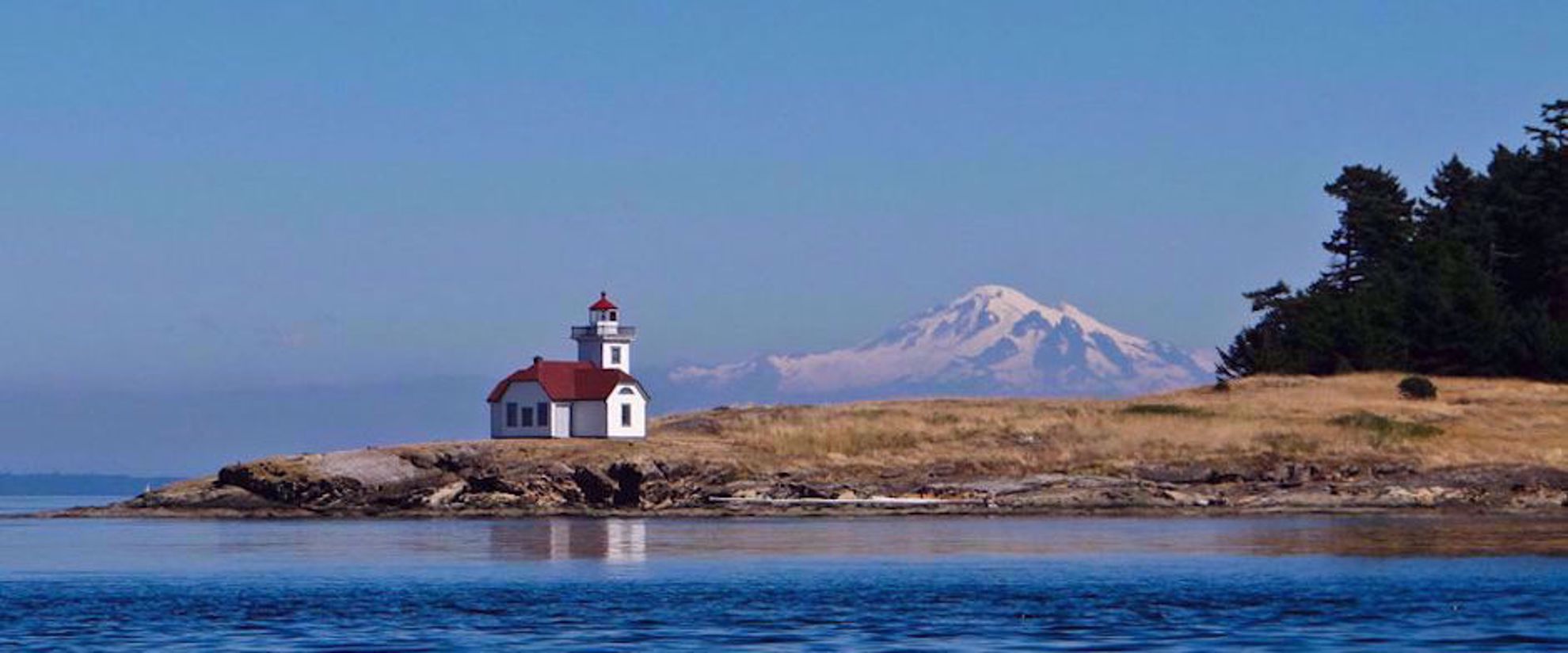 snow capped mountain and lighthouse by water
