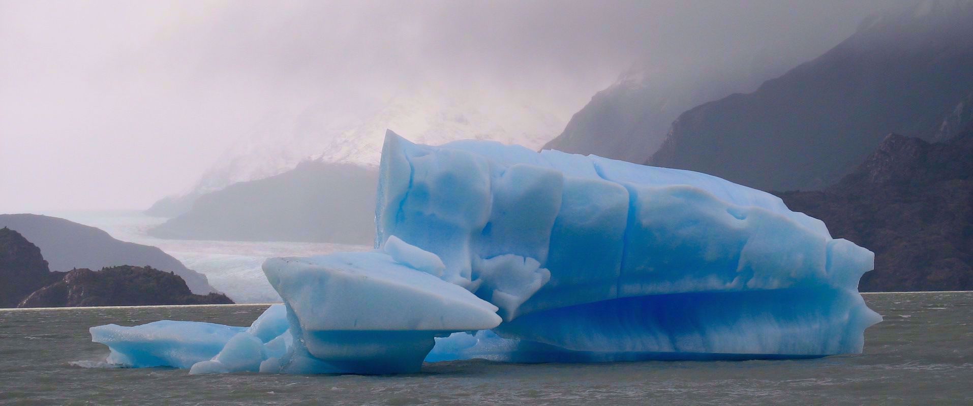 blue Iceberg floating in lake grey