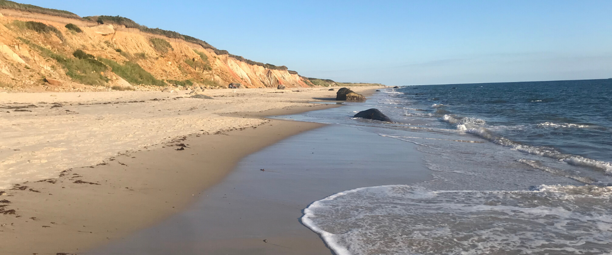 beautiful beach shot of cape cod. the water is lapping up on the sand, the sky is blue, and life is good