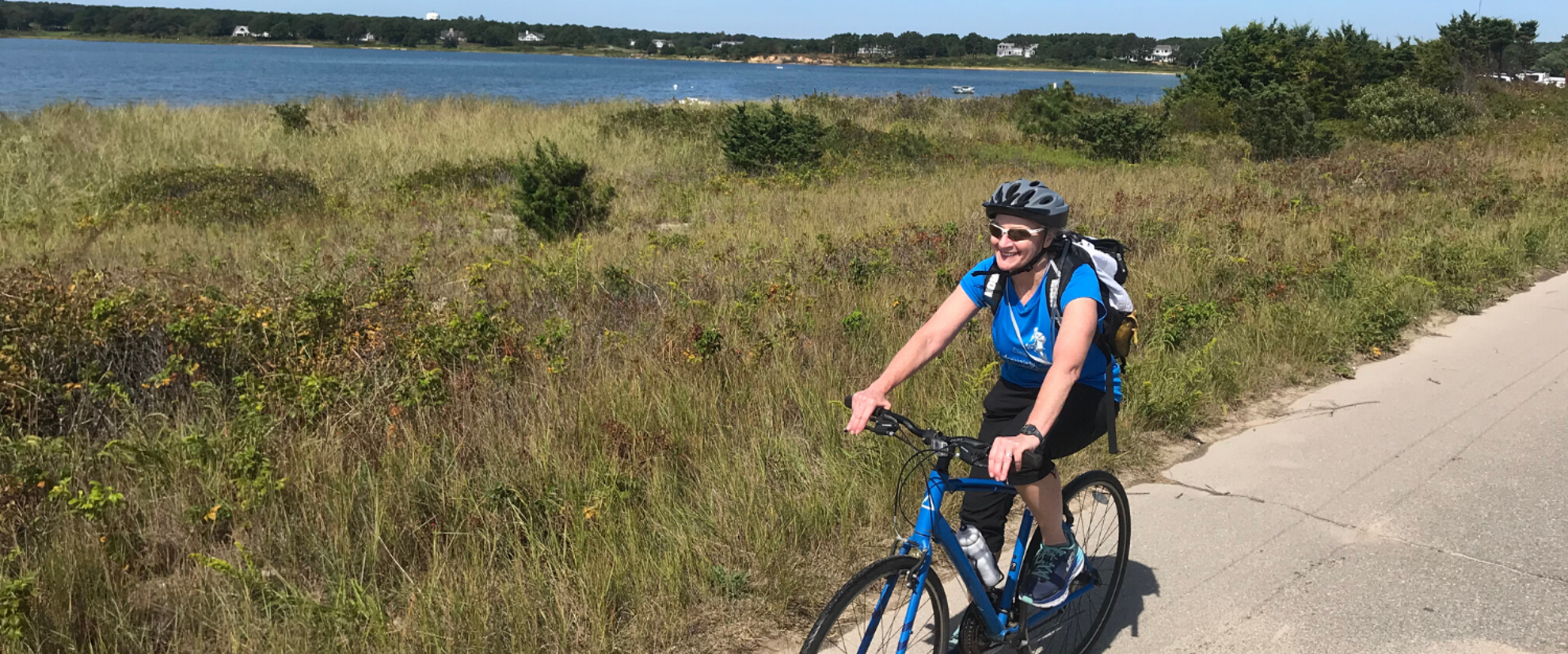 Cape cod is a perfect multisport adventure! This is a photo of  woman biking happily along the coast