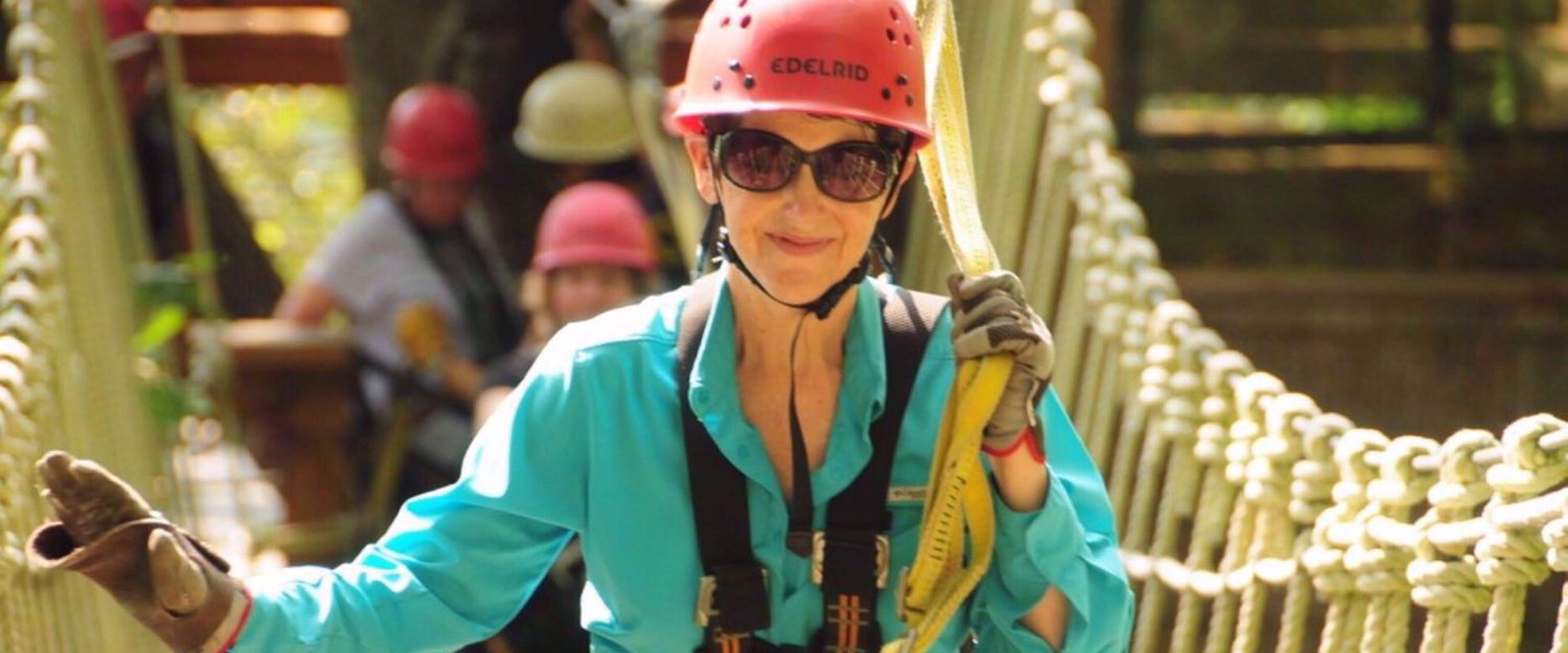 Woman crossing suspension bridge, smiling with red helmet