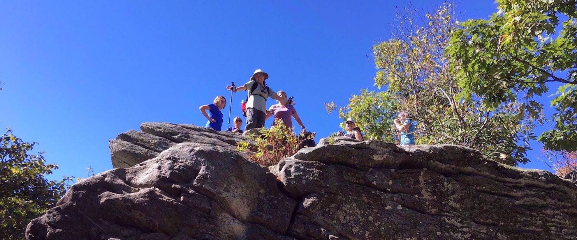 Women hiking Appalachian trail, standing on rock looking down and smiling
