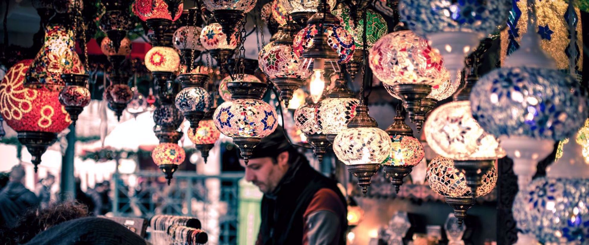 Glass lamps hanging in stall in Istanbul Bizarre, merchant in background