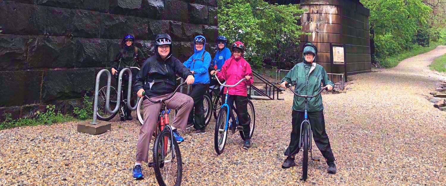 women in raincoats on bikes smiling on bike path in harpers ferry