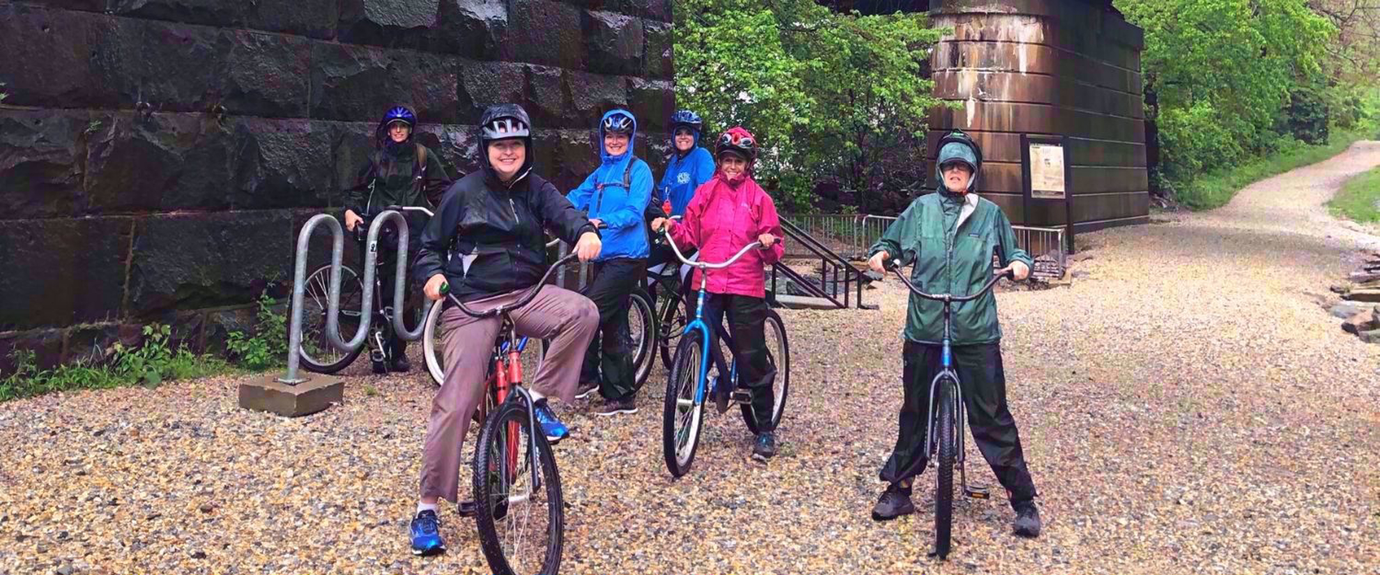 women in raincoats on bikes smiling on bike path in harpers ferry